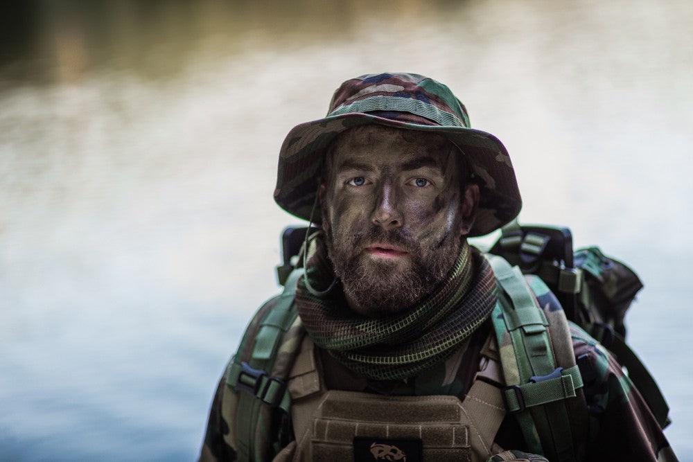 Rugged military man in tactical boonie hat with dark dirt on face