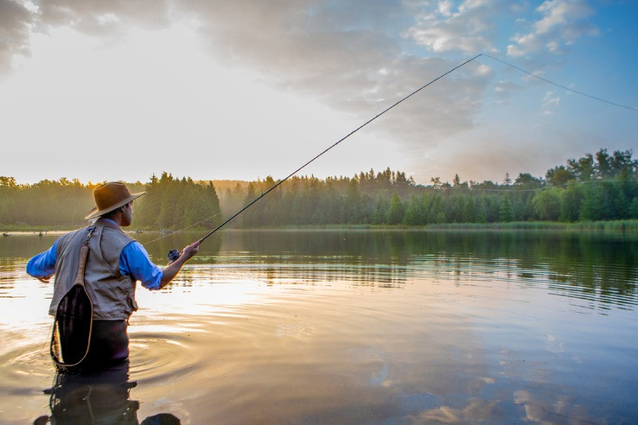 Man with hat fishing in water at sunset