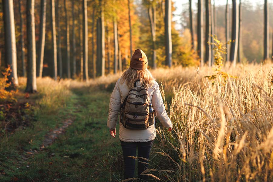 A woman is hiking in a forest, wearing a backpack