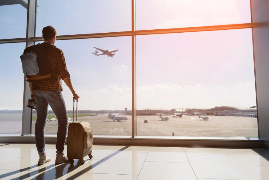 Man standing in airport and looking at aircraft flight through window